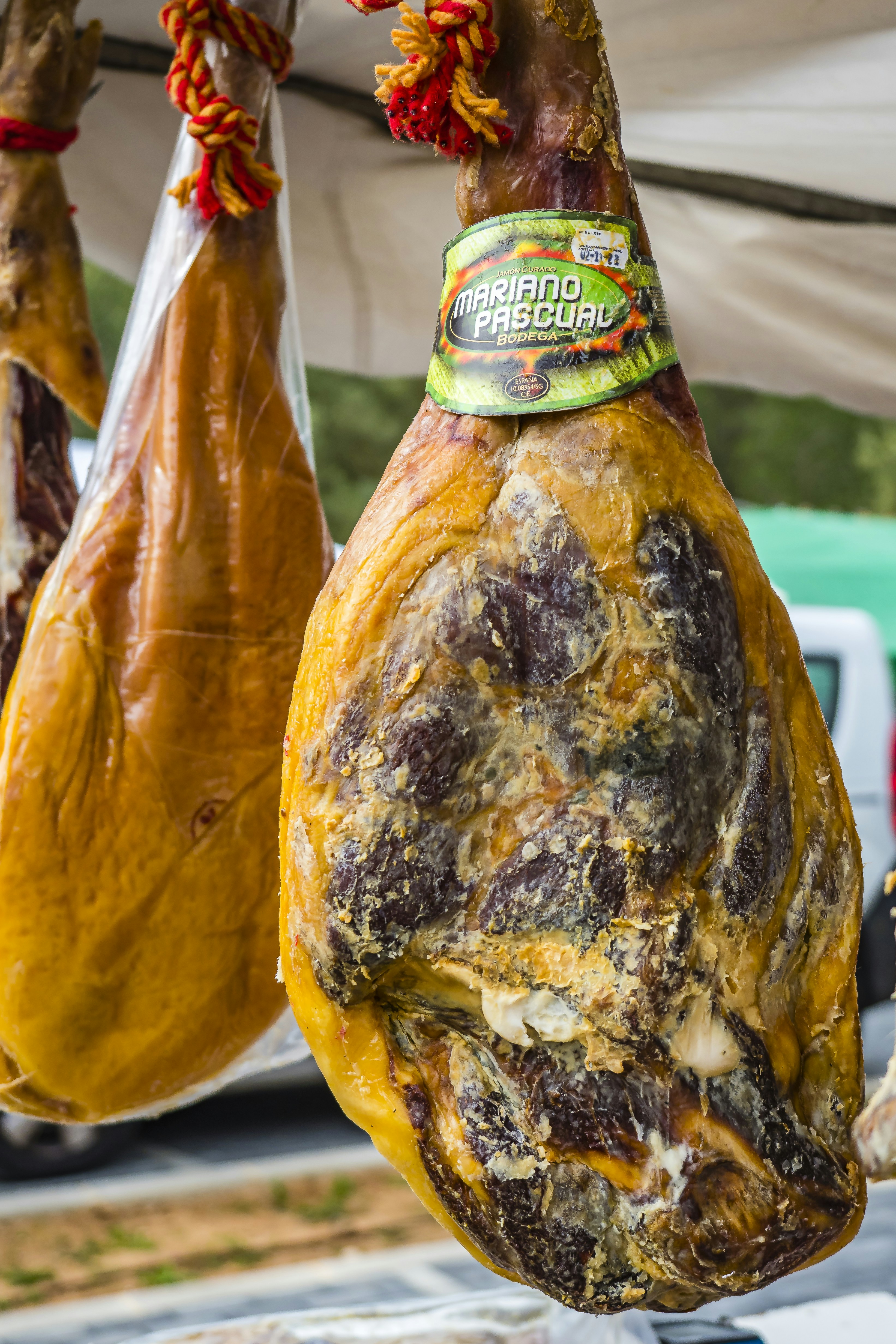 Cured ham leg hanging with visible mold and patina, labeled with producer mark`