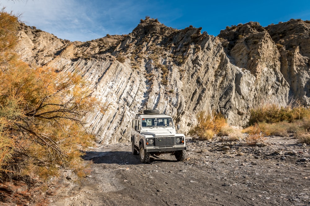 a white truck parked on a dirt road in front of a rocky mountain