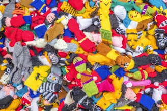 A colorful assortment of knitted socks, featuring a variety of designs and patterns. Each sock is made from vibrant yarns, displaying a mix of stripes, polka dots, and character faces, creating a lively and playful scene.