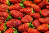 A pile of fresh, ripe strawberries with bright red skin and green leaves. The strawberries are densely packed, showcasing their plump and juicy texture.