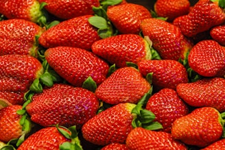 A pile of fresh, ripe strawberries with bright red skin and green leaves. The strawberries are densely packed, showcasing their plump and juicy texture.