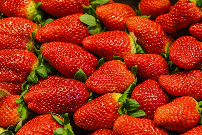 A pile of fresh, ripe strawberries with bright red skin and green leaves. The strawberries are densely packed, showcasing their plump and juicy texture.