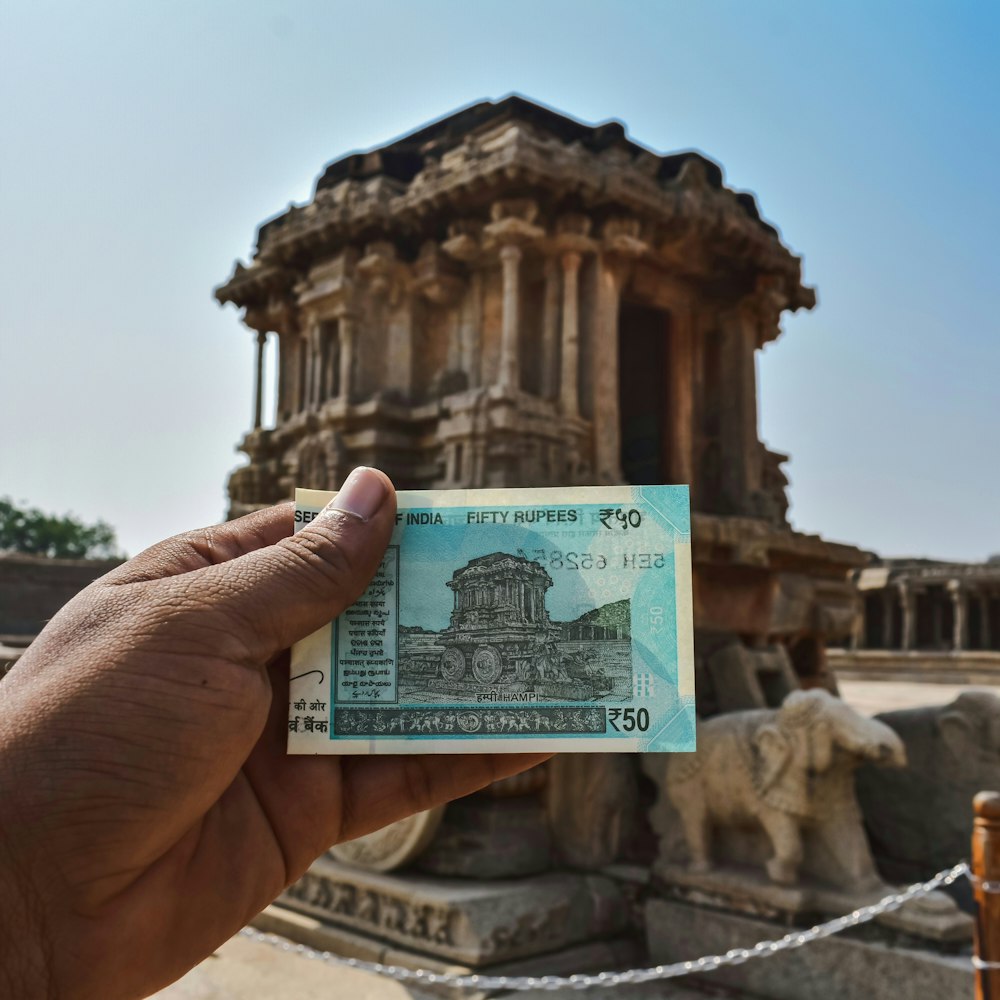 a hand holding a paper money in front of a building