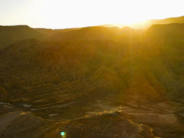 An operator scanning a rugged desert landscape using a metal detector, bathed in warm golden hour light.