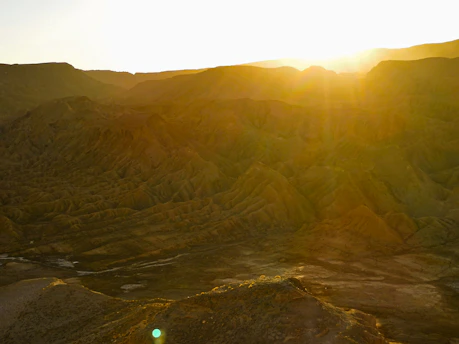 An operator scanning a rugged desert landscape using a metal detector, bathed in warm golden hour light.