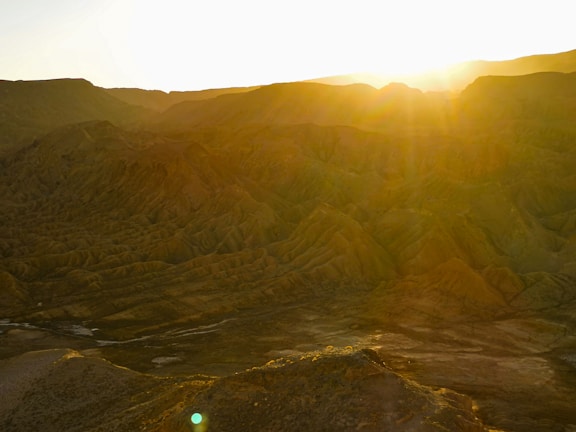 Sunset over the rugged desert landscape near Arad, with warm golden hues illuminating the rocky terrain.