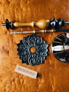 A wooden surface features several intricately designed wooden objects, including a black ornamental piece with detailed carvings. A wooden block with the word 'RESERVED' is prominently displayed. The arrangement suggests a carefully curated selection of decorative items.