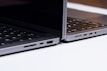 Two sleek, modern laptops positioned back-to-back on a light surface, showcasing the sleek edges and ports of the devices. The keyboards are partially visible, and the lighting highlights the metallic texture of the laptops.