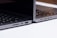 Two sleek, modern laptops positioned back-to-back on a light surface, showcasing the sleek edges and ports of the devices. The keyboards are partially visible, and the lighting highlights the metallic texture of the laptops.