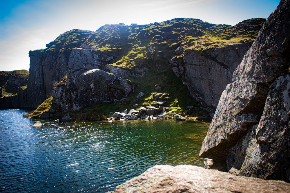 a body of water with a rocky cliff and a hill with a hill