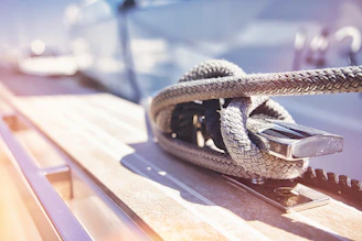 Close-up of hands adjusting nautical ropes on a wooden deck, sunlight sparkling on the sea.