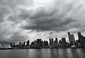 A moody black-and-white photo of a city skyline with stormy clouds overhead.