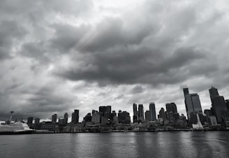 A moody black-and-white photo of a city skyline with stormy clouds overhead.