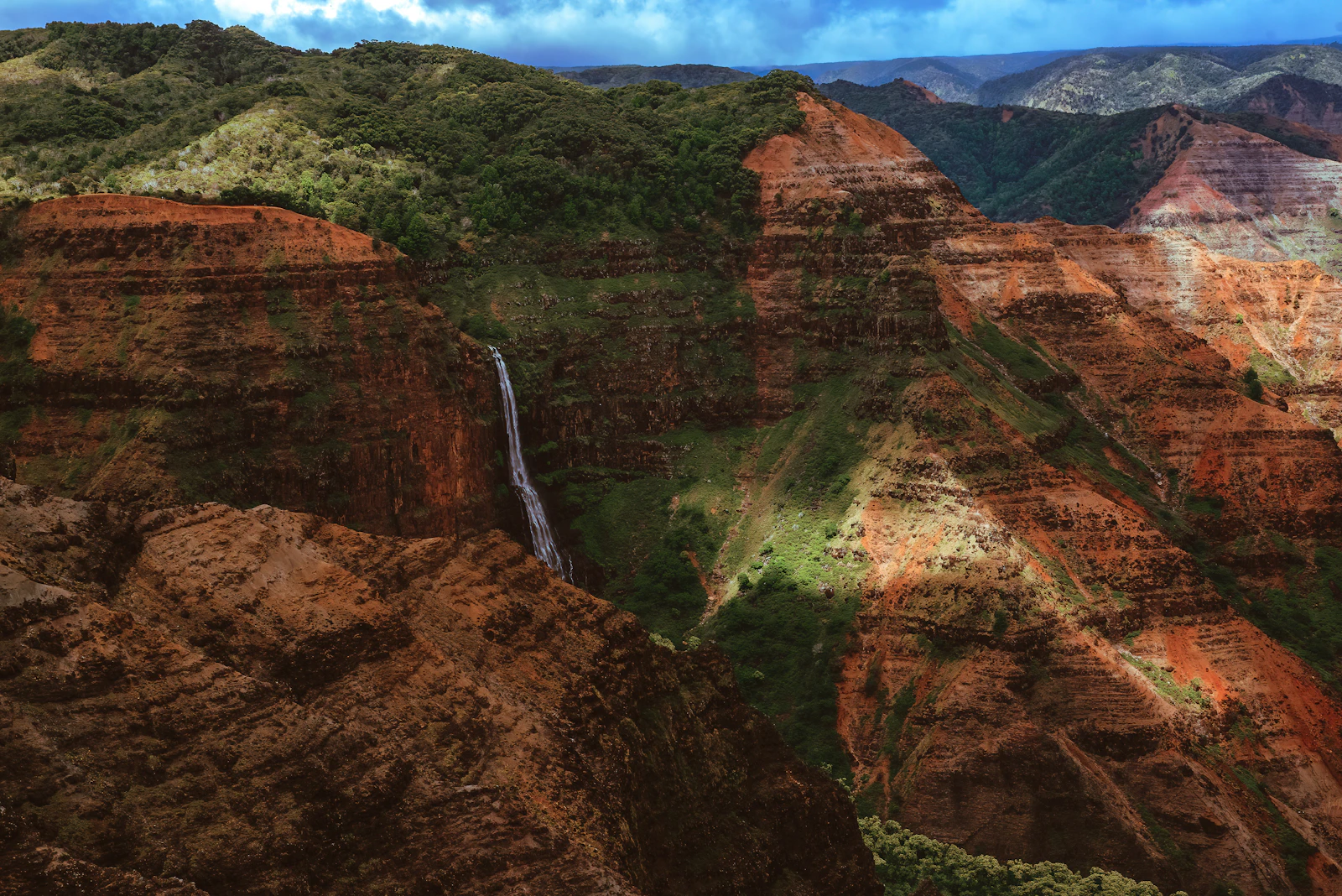 Waimea Canyon auf Kauaʻi mit roten Felswänden und Wasserfall