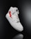 A white high-top sneaker prominently displayed against a dark background. The shoe features a distinctive red lightning bolt design on the side and is styled with white laces. The overall look is clean and modern, highlighting the shoe's sleek design and details.