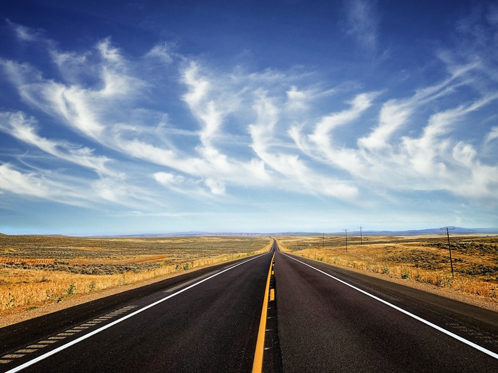 a long straight road with a blue sky and clouds