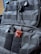 A close-up view of a black tactical backpack featuring multiple straps and Velcro patches. Attached to the backpack is a small, red pendant in the shape of a stylized wolf head.