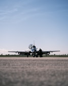 A small aircraft is parked on a runway with an overcast sky above. A solitary person stands near the aircraft, possibly engaged in a pre-flight inspection or maintenance task.