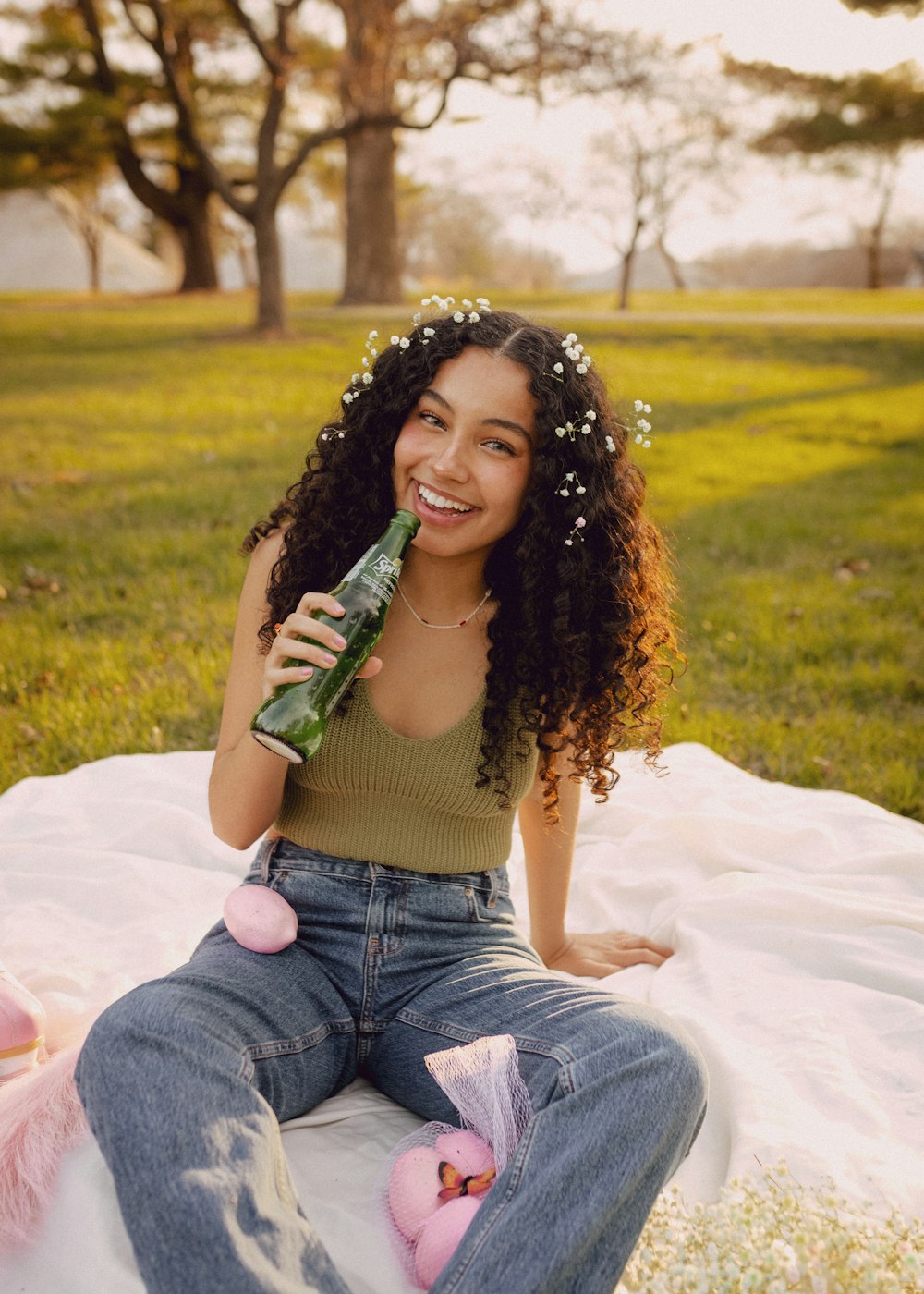 a woman sitting on a blanket holding a bottle of beer