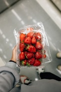 a hand holding a container of strawberries