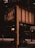 An urban scene featuring a large, industrial metal bridge structure with riveted beams. Below the bridge, there is a busy street with a car passing by. In the background, commercial signs for a parking garage and a well-known donut shop are visible, along with a traffic light and streetlamps.