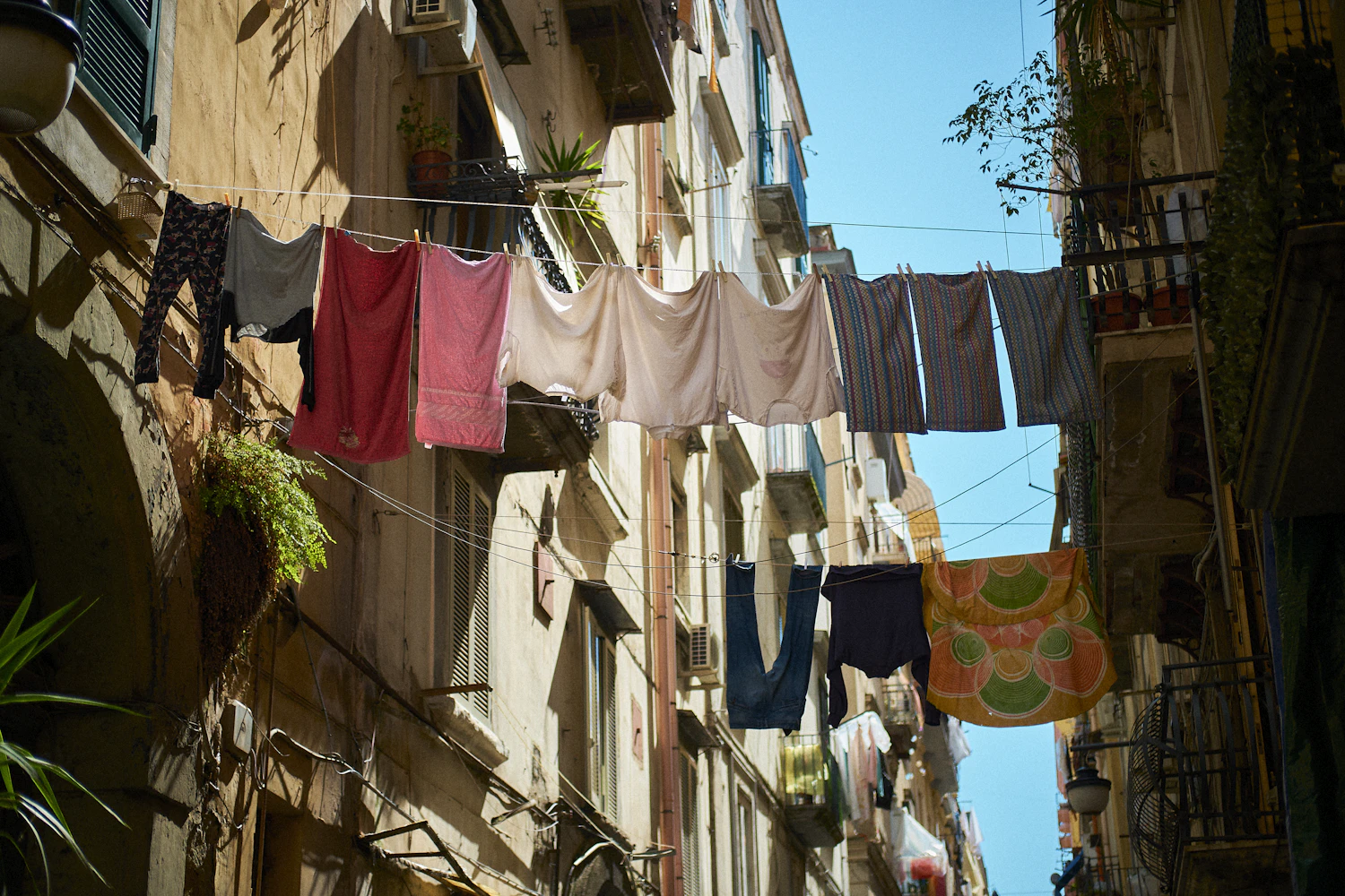 Shirts and towels drying on a line strung high across a street of tall old buildings