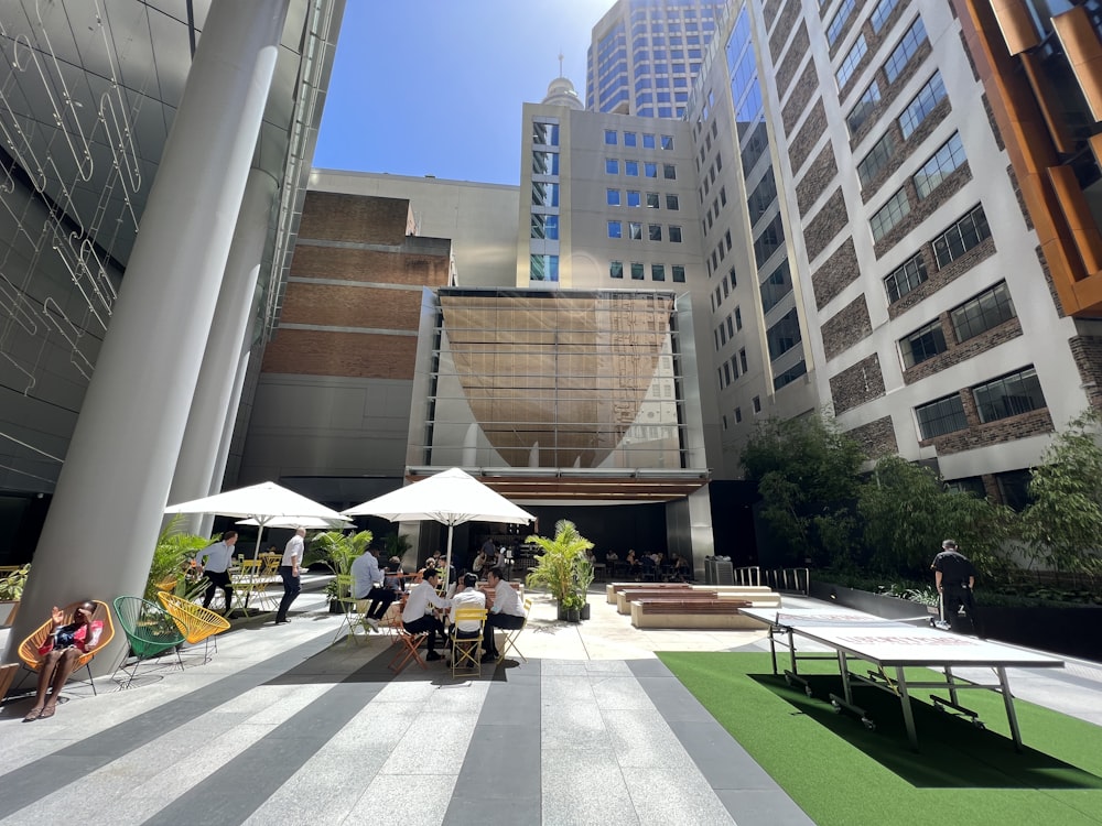 a group of people sitting at tables in a courtyard with tall buildings