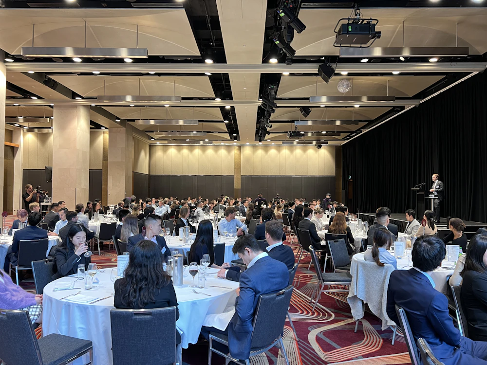 A speaker addressing a ballroom of seated guests at a corporate dinner