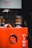 Two black coffee cups with orange text reading 'Freshly Ground Coffee' sit on a bright red fire extinguisher box. The background features a Dandenong Market sign.
