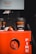 Two black coffee cups with orange text reading 'Freshly Ground Coffee' sit on a bright red fire extinguisher box. The background features a Dandenong Market sign.