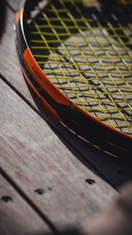 A close-up of a tennis ball resting on a wooden bench, with a racket nearby.