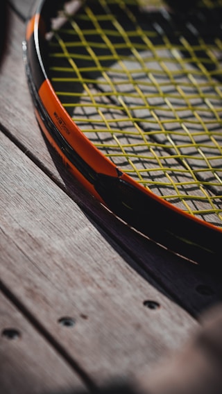 Close-up of a professional tennis racket with fresh twine, resting on a textured court surface.