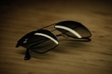 Close-up of sleek aviator sunglasses resting on a wooden table in natural sunlight.
