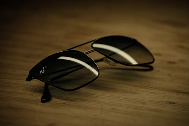 A pair of sunglasses with bright reflective lenses, laying next to a textured key chain on a sunlit wooden table.
