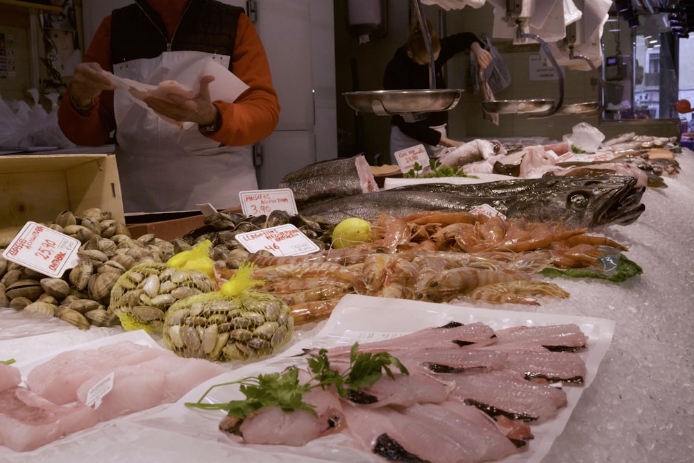 Una persona parada junto a una mesa llena de pescado y otros alimentos