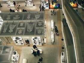 An aerial view of a modern retail store interior featuring neatly arranged displays of clothing, accessories, and mannequins. The store is well-lit with a sleek design, and several shoppers are visible browsing the merchandise. Glass and metal elements contribute to the contemporary aesthetic.