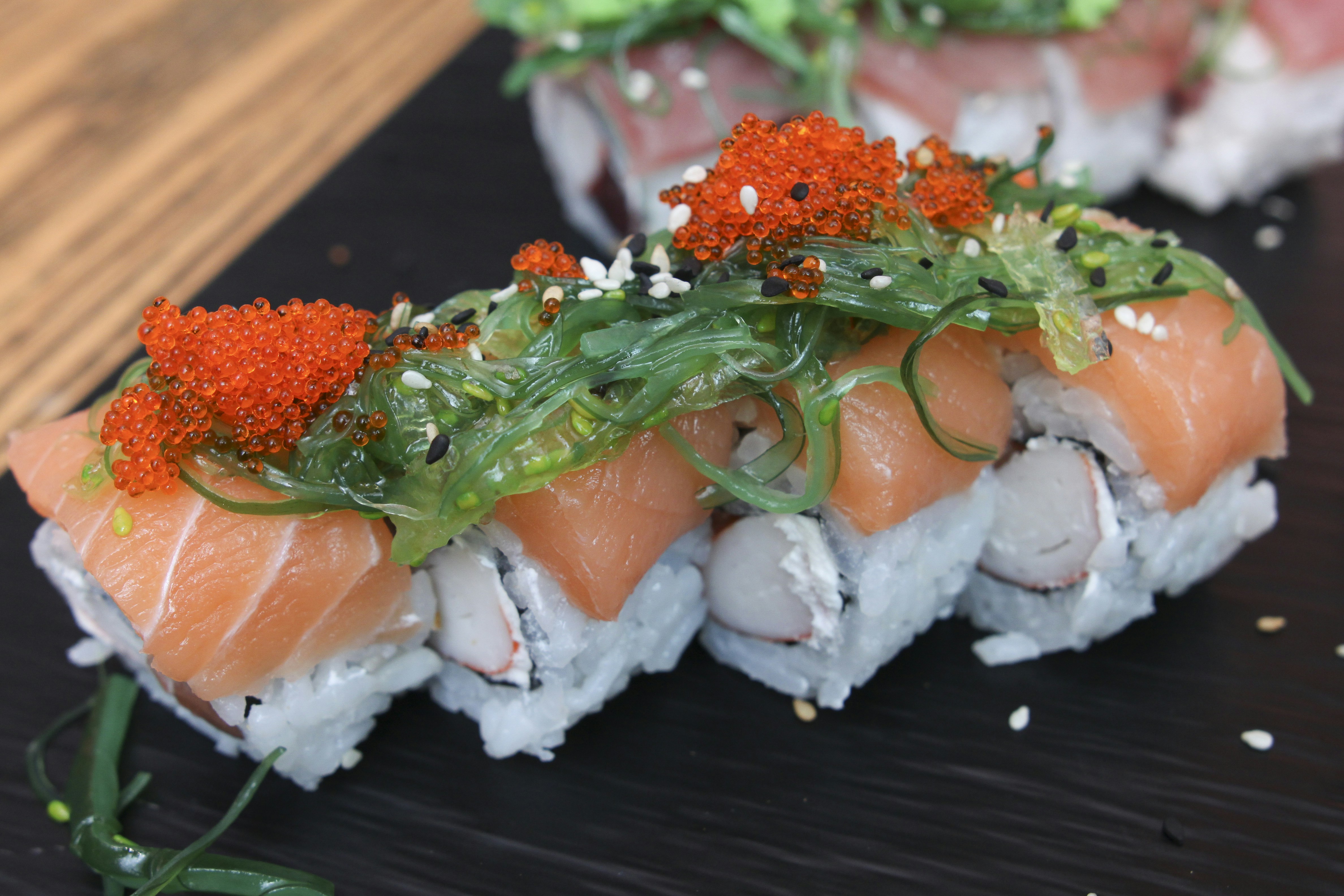 a plate of sushi, Set of Salmon maki sushi decorated with caviar and served on ceramic black plate 