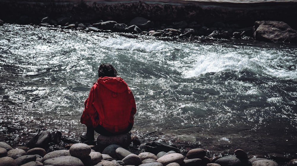 a person sitting on a rocky shore looking at a river
