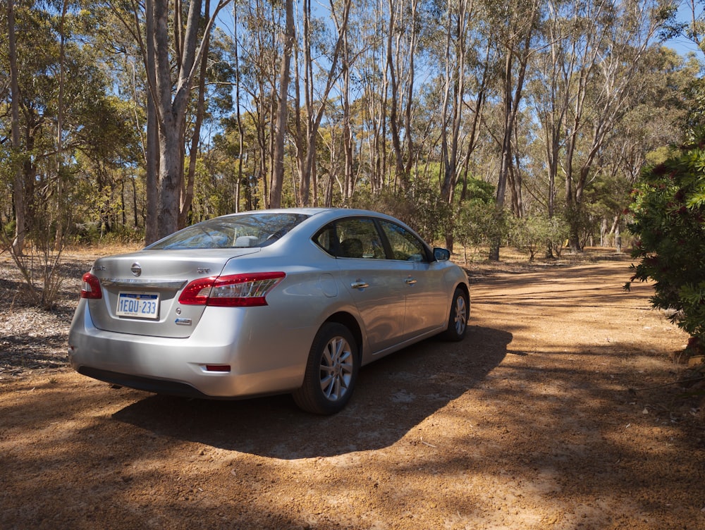 a silver car parked on a dirt road surrounded by trees