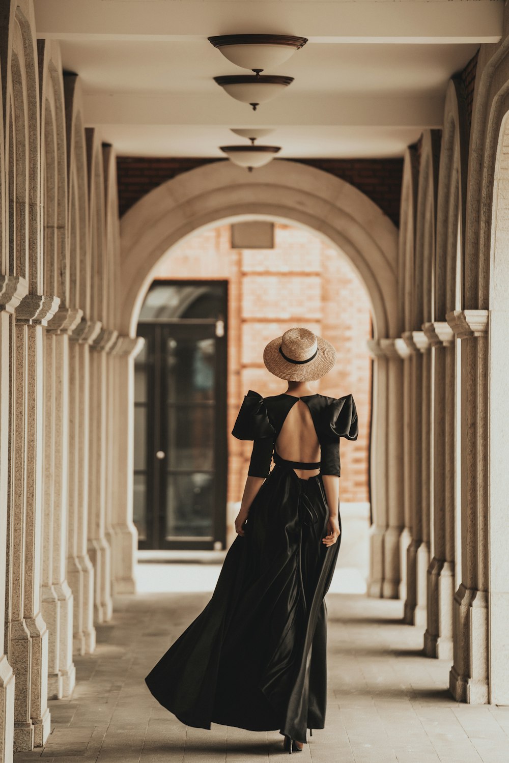 a woman in a black dress and hat in a room with pillars