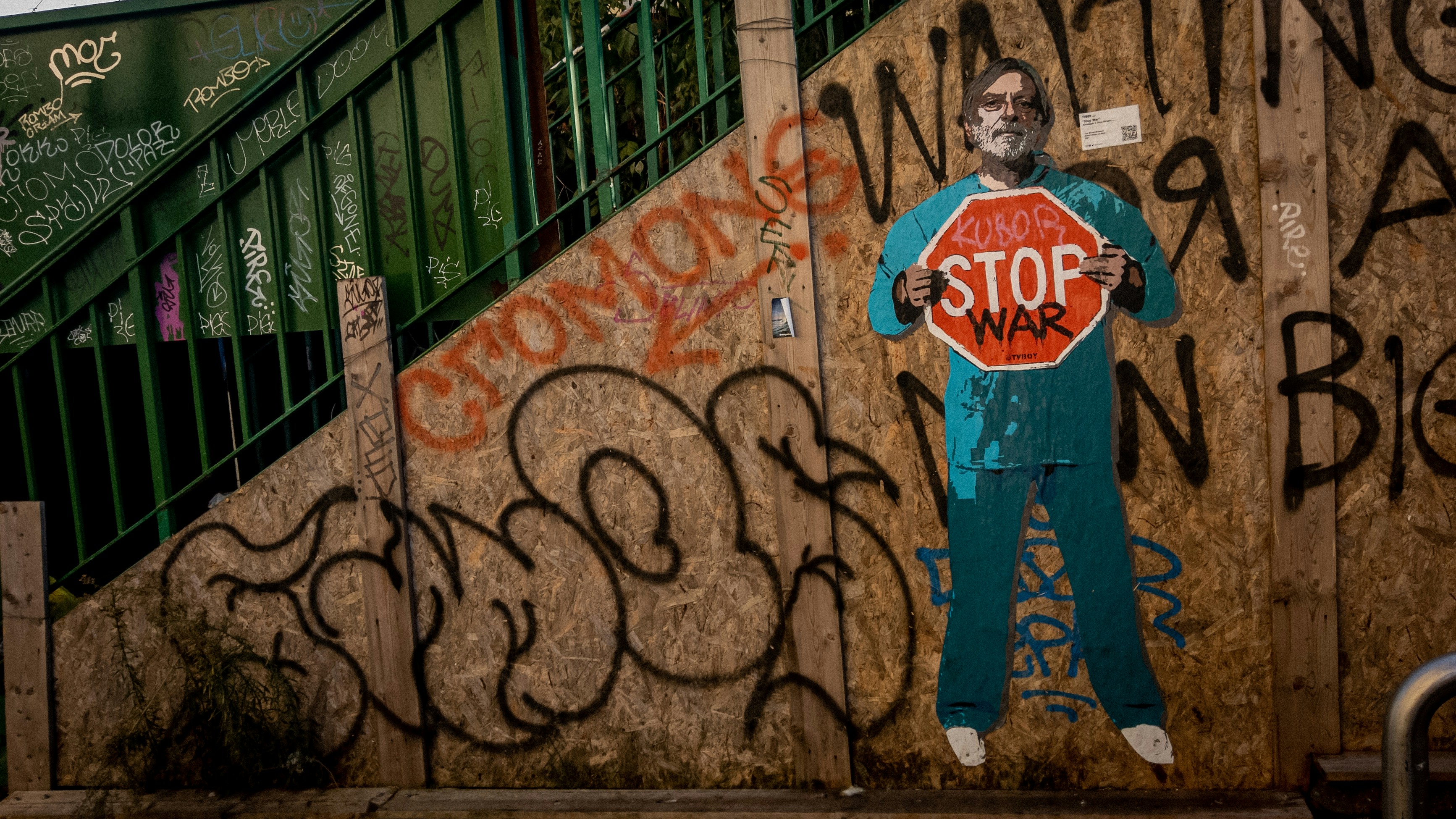 a person with a beard and mustache standing in front of a wall with graffiti