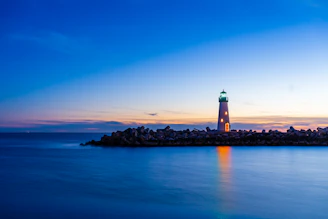 A serene lighthouse standing tall against a navy blue twilight sky, golden beams of light casting warmth over calm waters.