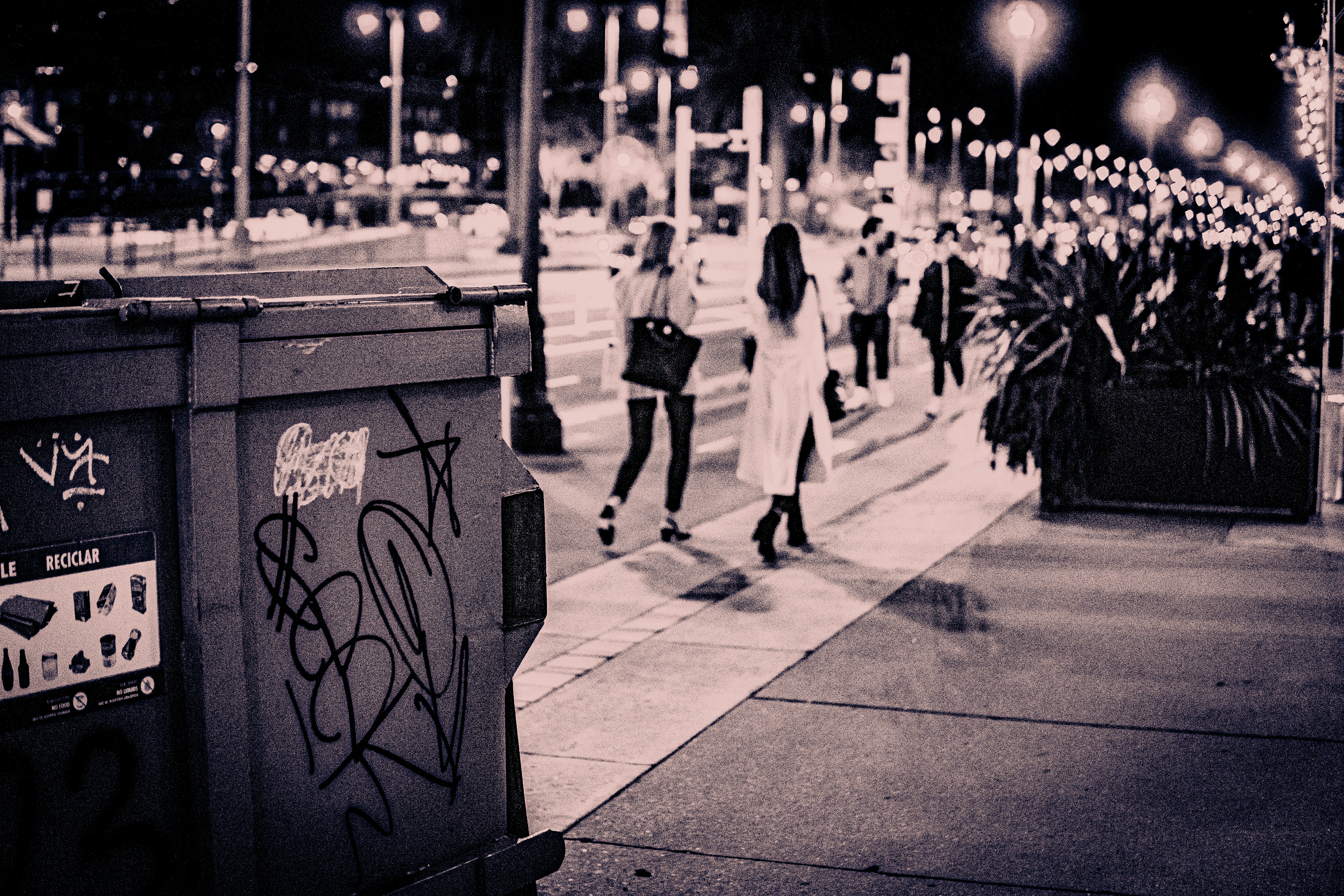a couple of women walking down a sidewalk at night