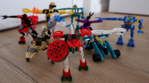 A group of colorful, articulated robot figures made from interlocking plastic pieces is arranged on a wooden floor. Each figure features distinct colors and shapes, with some resembling vehicles or animals equipped with mechanical limbs. The scene is playful and dynamic, showcasing a variety of textures and designs.