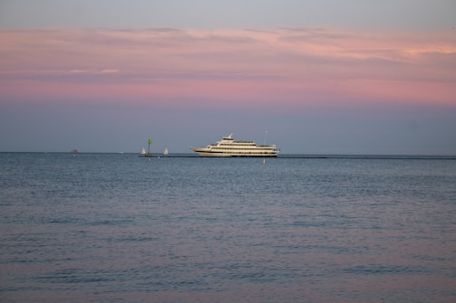 A sleek blue n blue yacht cutting through calm sea waters under a golden sunset.
