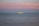 A large yacht is sailing on calm waters under a pastel-colored sky with shades of pink and blue. The horizon is dotted with a couple of small sailboats in the distance, adding depth to the serene seascape.