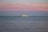 A large yacht is sailing on calm waters under a pastel-colored sky with shades of pink and blue. The horizon is dotted with a couple of small sailboats in the distance, adding depth to the serene seascape.