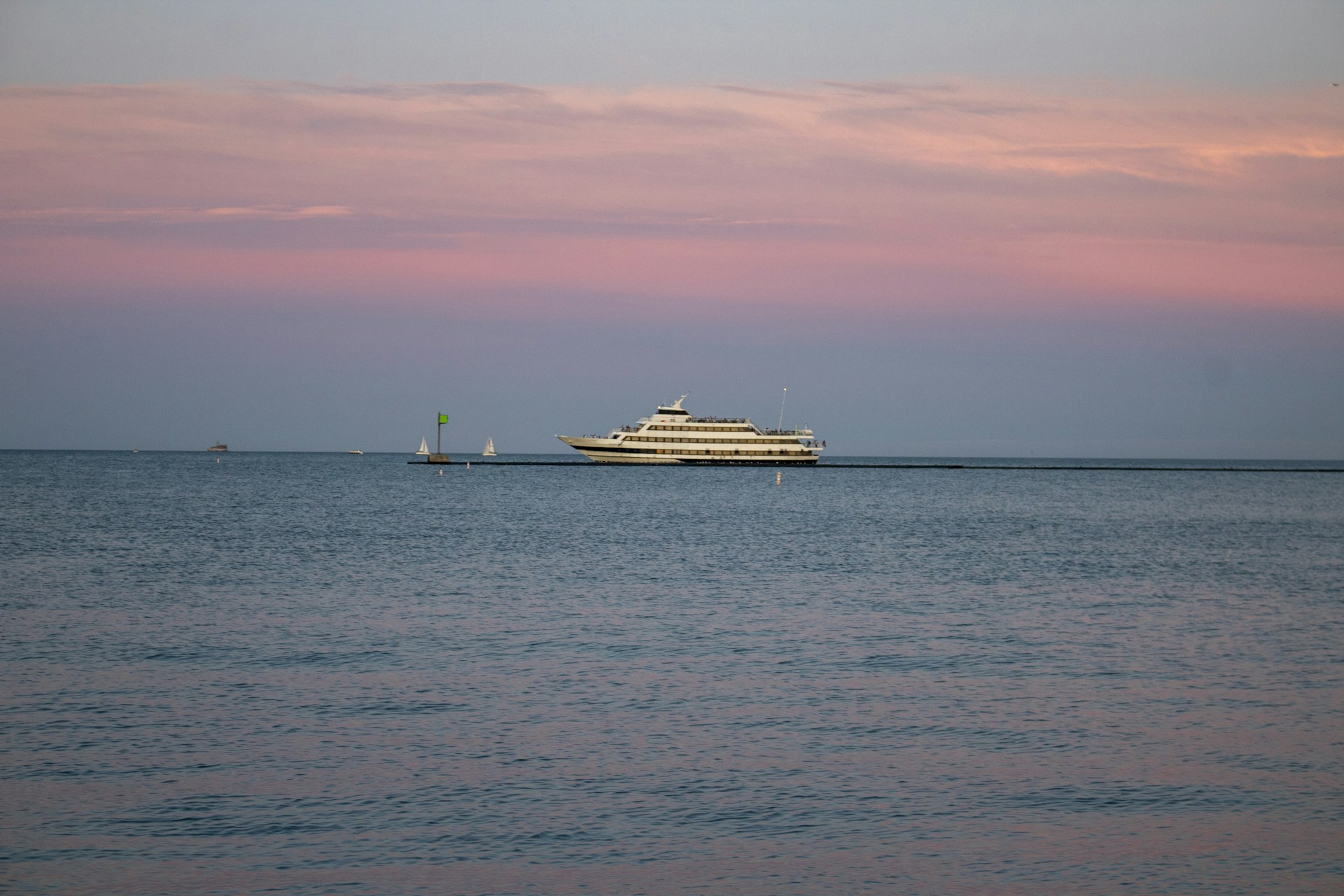 A sleek yacht cutting through calm blue waters under a clear sky at sunset.