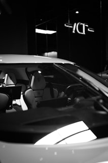 A sleek, modern car interior is visible through the windshield. The seats appear luxurious with a distinctive logo or emblem on the headrests, and a dashboard with advanced controls and screens.