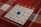 A bingo card is placed on a red and white plaid tablecloth. The card has columns labeled B, I, N, G, and O, each filled with numbers. A blue transparent marker is placed on the number 22 under the N column.